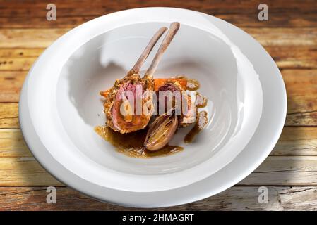 Costolette di agnello farcite di fegato al forno con scalini in piatto bianco su tavola di legno Foto Stock