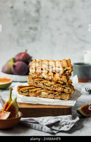 Cibo estivo sano e naturale. Sandwich con pane integrale, prosciutto, fichi e formaggio brie su tovagliolo in legno su sfondo grigio. Sano Foto Stock