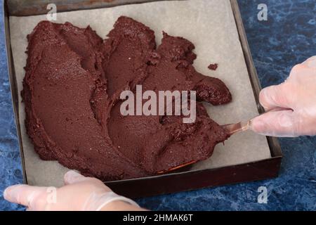 Pasta di brownie di formaggio è disposta in una muffa metallica. Il processo di fare un brownie formaggio. Sfondo di marmo blu. Primo piano. Foto Stock