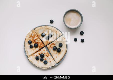 Pancake con mirtilli su un tavolo bianco con una tazza di caffè Foto Stock