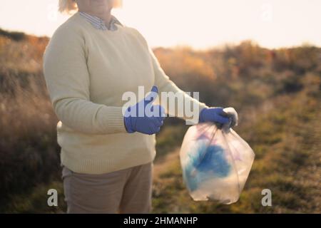 Giorno della terra. Purezza della natura. Donna pulup volontario attivista in guanti di gomma mano mette un sacchetto di plastica spazzatura in un sacco di rifiuti, raccogliendo rifiuti Foto Stock