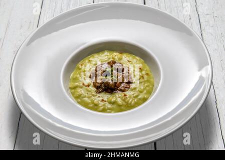 Risotto di verdure con stufato d'anatra, in piatto bianco su tavolini di legno bianco Foto Stock