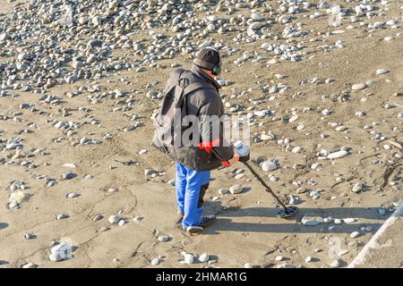 Uomo con un metal detector su una spiaggia di sabbia rocciosa dopo la tempesta Foto Stock
