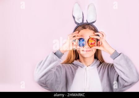 Ragazza in orecchie conigliate di coniglio sulla testa con uova colorate su sfondo rosa. Allegro sorridente bambino felice. Banner delle vacanze di Pasqua Foto Stock