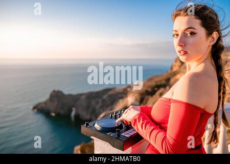 Le mani femminili del DJ suonano la musica mescolando e graffiando durante la festa serale con sfondo marino e caldo tramonto morbido. Primo piano di una console DJ controllata da Foto Stock