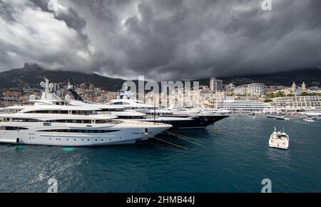 Molti grandi yacht si trovano nel porto di Monaco a causa delle tempeste, la montagna è sullo sfondo, bordo lucido del motoscafo, megayachts sono ormeggiati Foto Stock