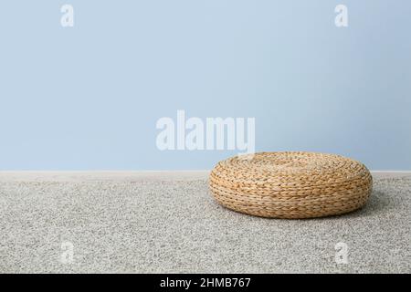 Pouf in rattan su tappeto grigio vicino alla parete blu Foto Stock