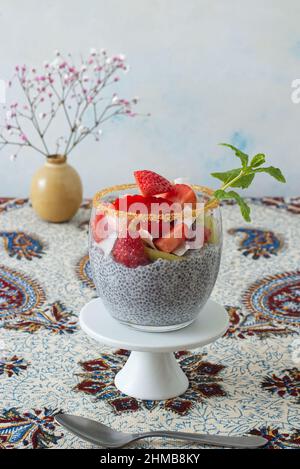 Vista ad angolo basso del dessert chia budino con bacche estive, fragole, kiwi e fette di cocco, impreziosito da un rametto di menta. Nessuna gente. Foto Stock