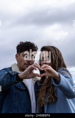 Foto di una coppia mista che ride e fa il cuore forme con le mani all'aperto Foto Stock