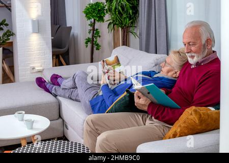 La coppia anziana era adorabile e riposava e leggeva sul divano di casa. Tempo libero nei giorni dei pensionati. Foto Stock