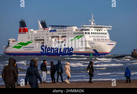 05 febbraio 2022, Meclemburgo-Pomerania occidentale, Warnemünde: Gli escursionisti guardano il traghetto StenaLine 'shane' entrare nel canale marittimo di Rostock dalla spiaggia. Foto: Jens Büttner/dpa-Zentralbild/ZB Foto Stock