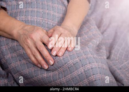 Le mani della vecchia donna riposano sopra la plaid. Foto Stock