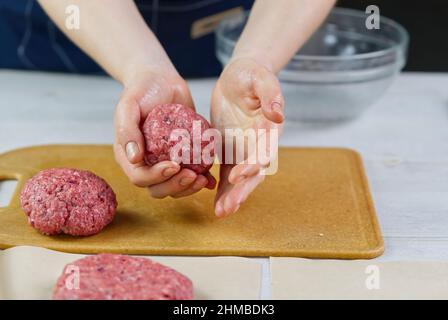 Mano della donna che forma una carne di manzo per una festa di hamburger. Porzionamento carne macinata. Hamburger fatti in casa. Fare il cibo a casa. Foto Stock