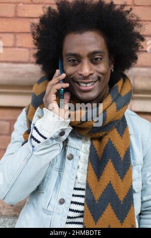 Ritratto di uomo afroamericano sorridente con look moderno e acconciatura afro parlando al telefono all'aperto. Foto Stock