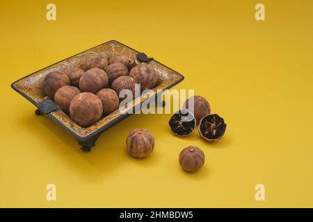 Sun Dried Organic Loomi o Black Lime, Black Lemon, Omani Lemon in piatto d'epoca orientale su sfondo giallo. Cucina mediorientale Foto Stock