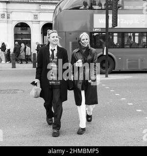 Londra, Greater London, Inghilterra, febbraio 05 2022: Due donne alla moda, una con un corpetto sorridente e fremito, camminano attraverso Bridge Street con un autobus Foto Stock