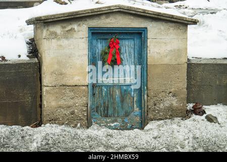 un capannone di città con porta dipinta blu peeling e una vacanza sempreverde bough con un arco rosso Foto Stock
