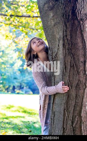 La ragazza giovane dà un abbraccio al suo albero preferito nel suo cortile Foto Stock