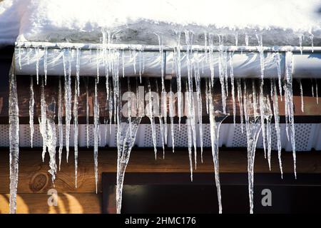 Molte ghiacciole appendono dal tetto e dal downpipe della casa di campagna. Fusione del ghiaccio. Sfondi primavera e inverno Foto Stock