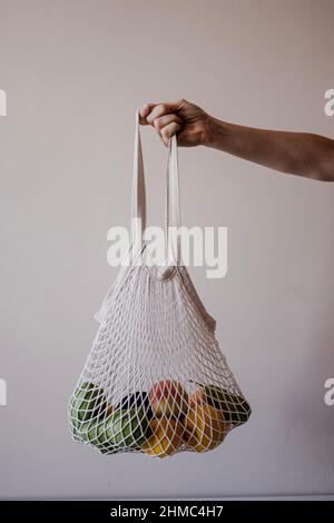 La ragazza sta tenendo una borsa eco-consapevole piena di frutta su sfondo chiaro. Foto Stock