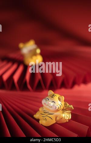 Scatto verticale di una figurina della tigre carina su una ventola pieghevole della carta su sfondo rosso Foto Stock