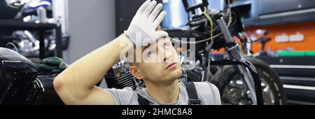 Stanco uomo che tiene la testa vicino alla motocicletta Foto Stock