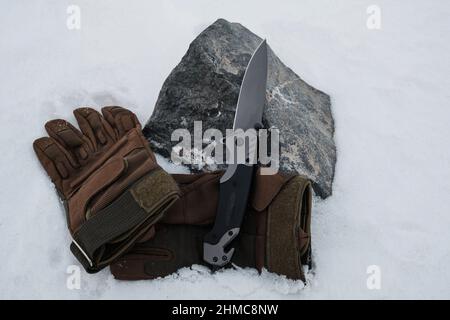 Guanti tattici e un coltello pieghevole nella neve Foto Stock