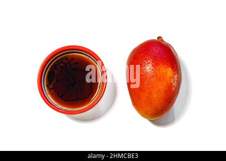 Fresco mango rosso-arancio succoso e tè in una ciotola rosso-arancione isolato su sfondo bianco, primo piano Foto Stock