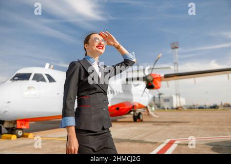 Gioioso assistente di volo donna in piedi all'aperto in aeroporto Foto Stock