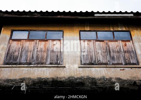 Esterno di un antico edificio con lichene nero su pareti di cemento e vecchia cornice di legno di finestre, decorate con vetro in alto. Tetto di costruzione di r Foto Stock