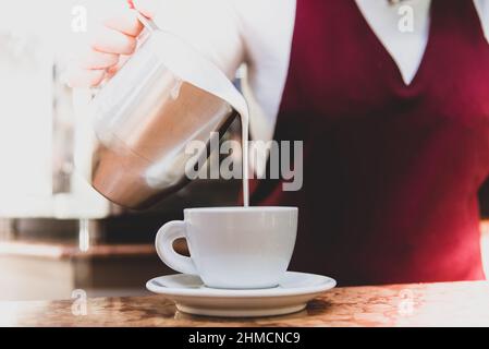 il barista versa il latte per preparare un cappuccino Foto Stock