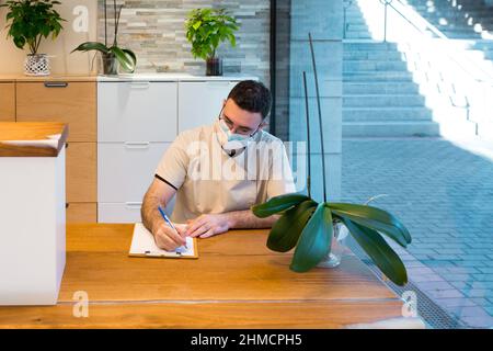 Uomo che indossa una maschera mentre lavora nell'area di ricevimento di un centro medico. Foto Stock