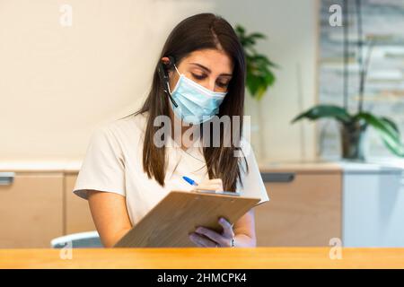 L'addetto alla reception prende appunti presso il centro medico Foto Stock