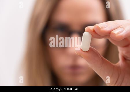 Primo piano della mano femminile che tiene la pillola bianca o capsula supplemento vitamina primo piano Foto Stock