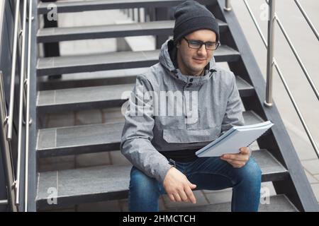 Ritratto Street style di bell'uomo di 30-35 anni all'aperto seduto sulle scale Foto Stock