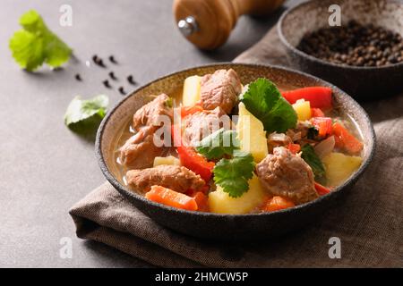 Stufato di manzo con verdure, patate, pepe, carota in ciotola su sfondo marrone. Cucina europea. Primo piano. Foto Stock