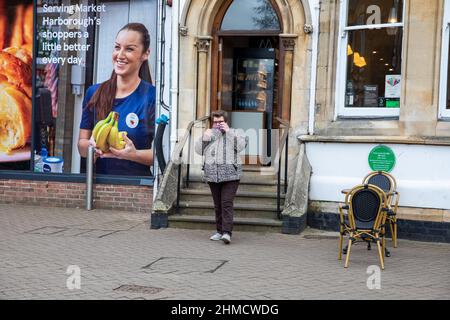 Una signora rimuove la sua maschera dopo aver lasciato caffe Nero in Market Harborough, Leicestershire, Regno Unito Foto Stock