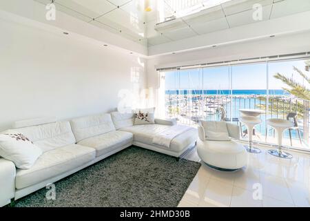 Un lussuoso soggiorno con un grande divano bianco che si affaccia sull'esclusivo porto di Puerto Banus nella Costa del Sol Foto Stock