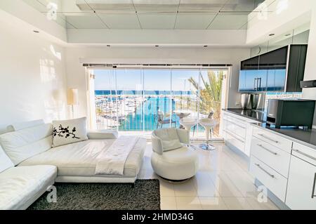 Soggiorno e sala da pranzo di lusso con ampio divano bianco affacciato sull'esclusivo porto di Puerto Banus, nella Costa del Sol Foto Stock