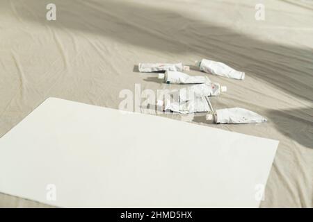 tubi di vernice acrilica tempera sparsi intorno sulla tavola di pittura vicino alla tela di carta. Foto di alta qualità Foto Stock