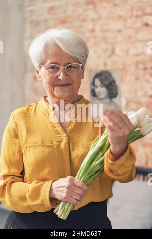 Nonni giorno nazionale Grandma con tulipani bianchi che mostrano una foto di Blur del suo giovane sé. Foto di alta qualità Foto Stock