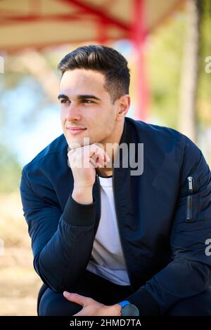 Giovane uomo bello in abiti casual seduto nel parco della città dopo aver giocato sport Foto Stock