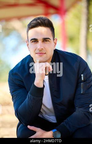 Giovane uomo bello in abiti casual seduto nel parco della città dopo aver giocato sport Foto Stock