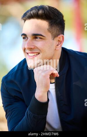 Giovane uomo bello in abiti casual seduto nel parco della città dopo aver giocato sport Foto Stock