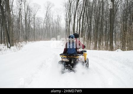 Uomo in quad accanto a una donna. Giovane coppia che fa attività invernali all'aperto, cavalcando un ATV nella foresta innevata Foto Stock