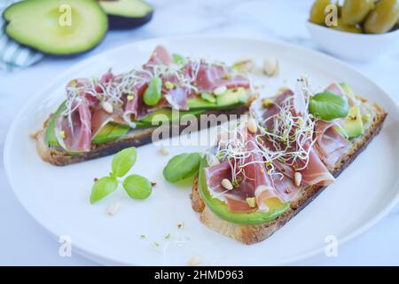 Panini a grani interi con fette di avocado, prosciutto o jamon, semi germinati ed erbe. Mangiare pulito, colazione sana. Vista dall'alto. Foto Stock
