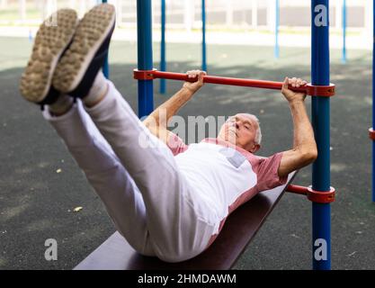 Palestra all'aperto. Formazione stradale sulle attrezzature sportive comunali. Uomo anziano pompa la stampa nel parco della città Foto Stock