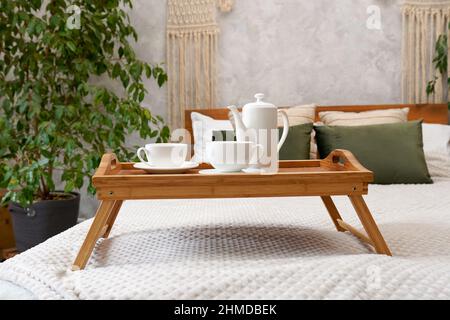 Tè verde alle erbe su un vassoio di legno in piedi sul letto in casa accogliente con piante verdi Foto Stock