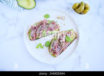 Panini a grani interi con fette di avocado, prosciutto o jamon, semi germinati ed erbe. Mangiare pulito, colazione sana. Appartamento vista dall'alto l Foto Stock