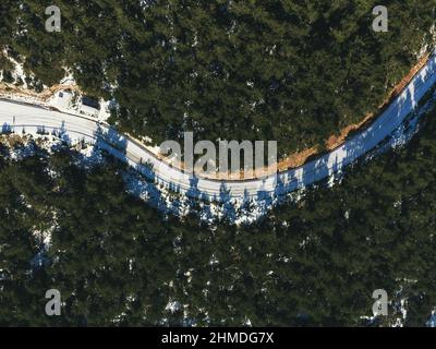 Vista dall'alto di una strada curva e nevosa tra i pini. Foto Stock